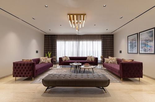 Symmetrical living room with three merlot velvet sofas, tufted ottoman, and layered gold chandelier