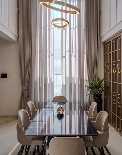 Dining table with dark marble top under tall sheer curtains and ring pendant lights
