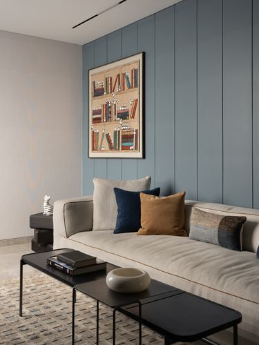 Beige sofa with navy and mustard cushions against blue slatted panel wall with framed art