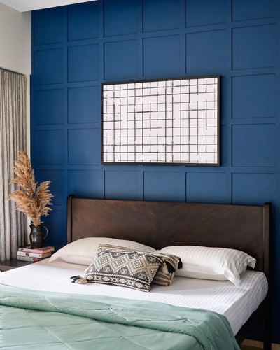 Bed with dark wood headboard against a blue paneled wall, framed grid art above