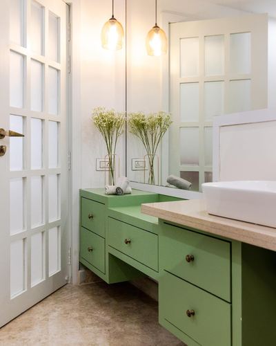 Green vanity with vessel sink and drawers beside white paneled door and pendant lights