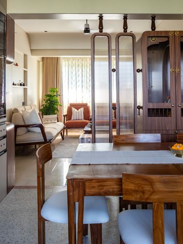 Wooden dining table in foreground with fluted glass partition separating living room beyond