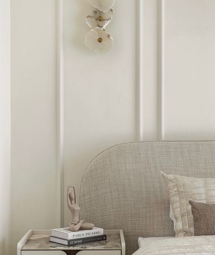 Cream bedroom corner with panelled wall, curved woven headboard, and stone-topped nightstand with books