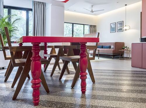 Red lacquered dining table with cane wooden chairs on terrazzo floor, living area beyond