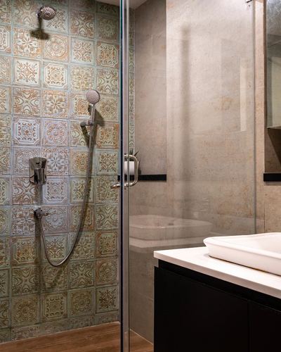 Bathroom with patterned tile shower behind glass and stone-clad vanity wall with black cabinetry