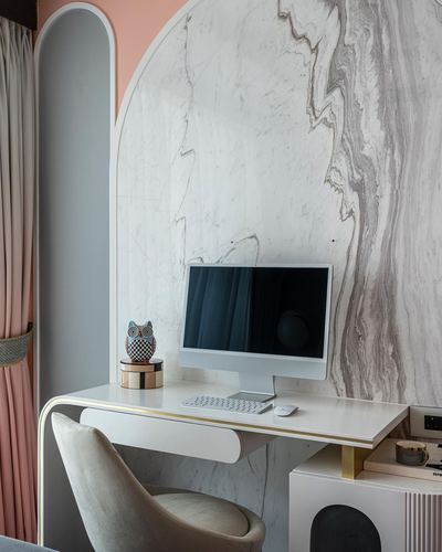 White desk with computer set against a veined marble arched wall, pink curtain beside.