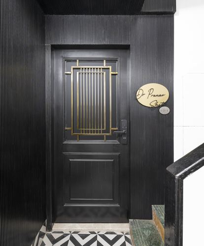 Black fluted entrance door with brass grille panel and oval nameplate beside chevron tiled floor