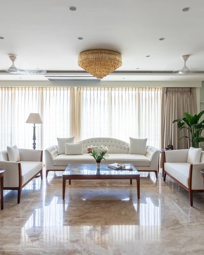 Symmetrical cream living room with tufted sofas around a marble-top coffee table under sheer curtained windows