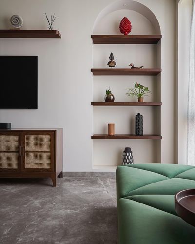 Living room with arched shelving niche, cane TV console, and green tufted ottoman