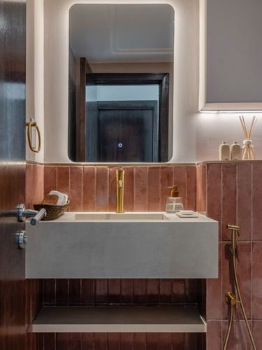 Bathroom with terracotta ribbed tile, backlit mirror, brass fittings, and concrete floating vanity