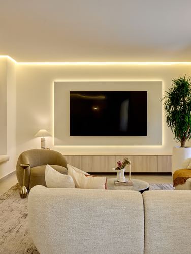 Neutral toned living room with backlit TV wall, wood console, boucle sofa and cane armchair