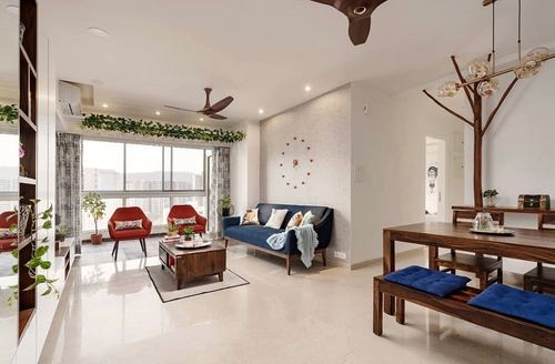 Open living and dining area with navy sofa, red accent chairs, wooden dining table and branch chandelier