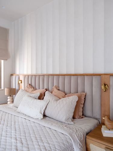 Bed with channel-tufted headboard, brass sconces, and layered pink and white pillows
