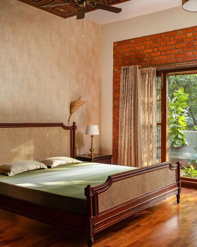 Wooden cane bed with olive linen in bedroom facing brick-framed glass door and garden