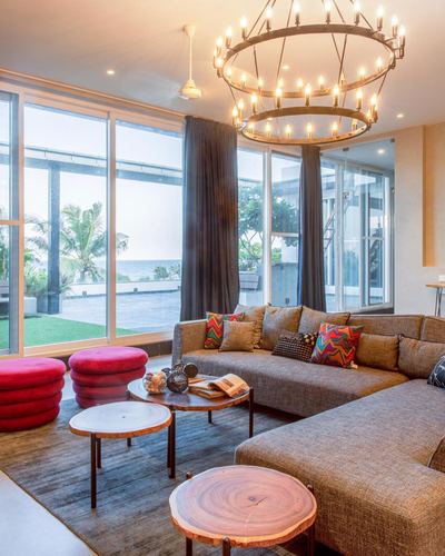 Living room with layered chandelier, sectional sofa, live-edge tables and sea view through glass walls