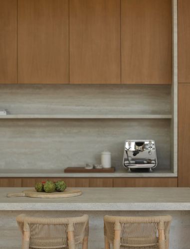 Minimalist kitchen with wood cabinetry, stone backsplash niche, espresso machine, and woven stools at island