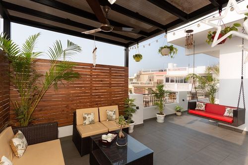 Rooftop terrace lounge with wicker sofas, red swing, wood slat screen, and plants under a pergola roof