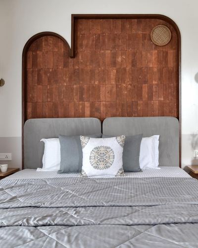 Bed with grey upholstered headboard set against an arched terracotta tile wall niche