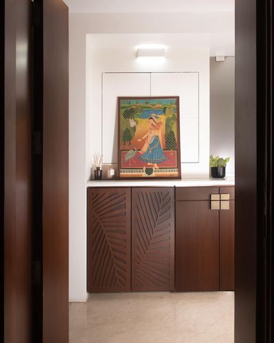 Foyer console with carved leaf-pattern wooden cabinets and a traditional painting, viewed through open door