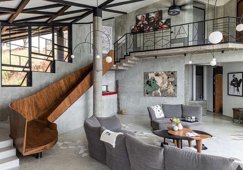 Double-height living room with wooden slide, concrete walls, grey sectional and mezzanine above