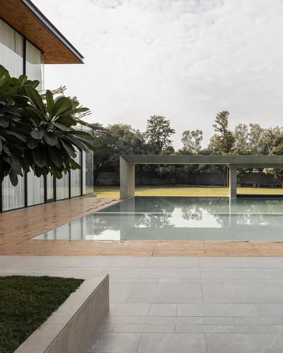 Modern house with glass facade beside a reflecting pool and concrete pergola, lawn beyond