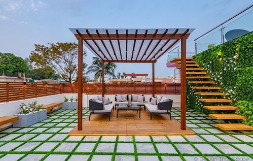Rooftop terrace with wooden pergola over grey wicker seating, grass-and-stone tiled floor, and green wall staircase
