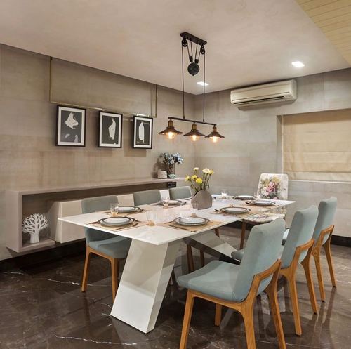 Dining room with white marble table, sage chairs, and industrial pendant lights over dark floor