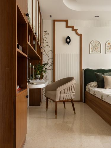 Bedroom corner with green upholstered bed, cane-backed chair, wooden desk, and arched decorative wall niche