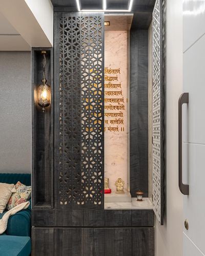 Pooja unit with dark jaali doors open to reveal a backlit stone panel with Sanskrit text and a small brass idol