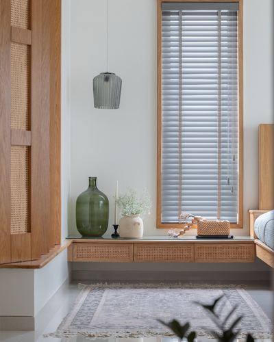 Window seat with cane drawers, glass bottle vase, and grey pendant lamp beside a louvred window