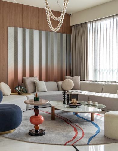 Living room with curved beige sofa, layered chandelier, and oval marble coffee tables on round rug.
