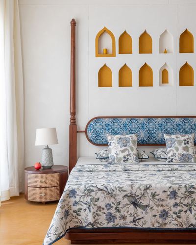Bedroom with four-poster wood bed, blue floral headboard, and mustard arched wall niches