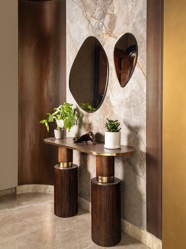Foyer console with two asymmetric mirrors on veined stone wall, fluted wood cylindrical legs