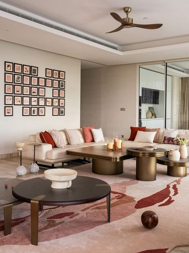 Neutral living room with curved sofas, layered round brass tables, and a gallery wall of small framed art