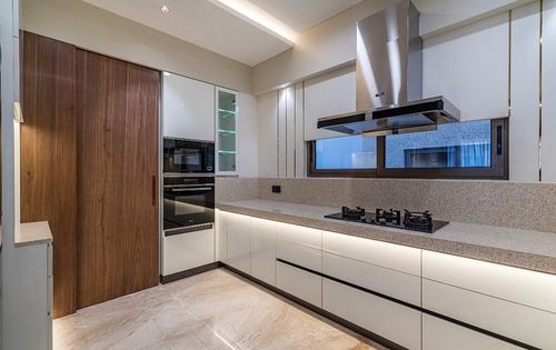 Modern L-shaped kitchen with white cabinetry, stone countertop, wood door and steel chimney hood