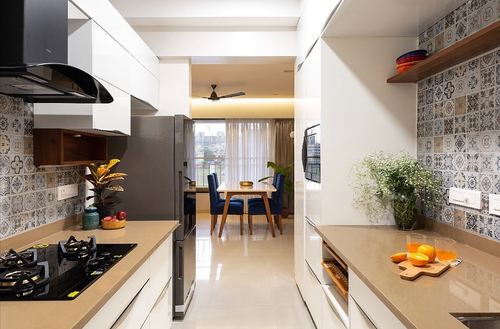Galley kitchen with patterned tile backsplash opening onto dining room with blue chairs