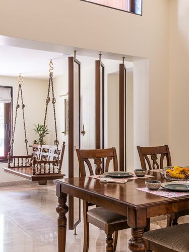 Wooden dining table with carved chairs beside a suspended wooden swing in a tiled foyer