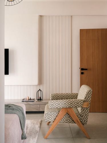 Geometric-print armchair with wooden legs beside fluted wall paneling and a wood door