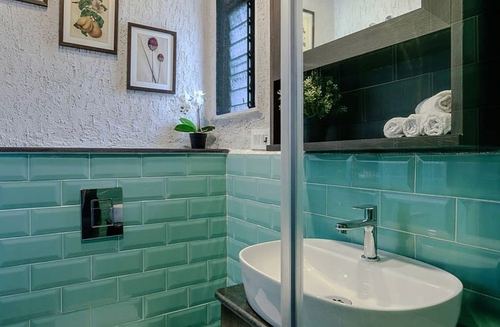 Bathroom corner with seafoam subway tile, white vessel sink, framed prints, and orchid on ledge