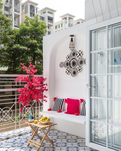 White balcony nook with arched wall niche, patterned plates, pink cushions, and bougainvillea against city view