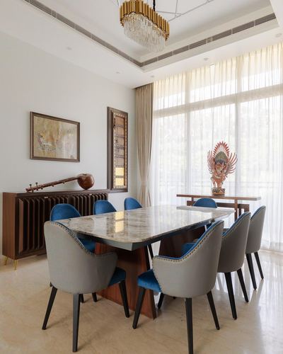 Dining room with marble table, blue and grey chairs, brass chandelier, and sheer curtains