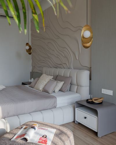 Bed with tufted headboard beneath sculpted wave-textured plaster wall and gold pendant lights