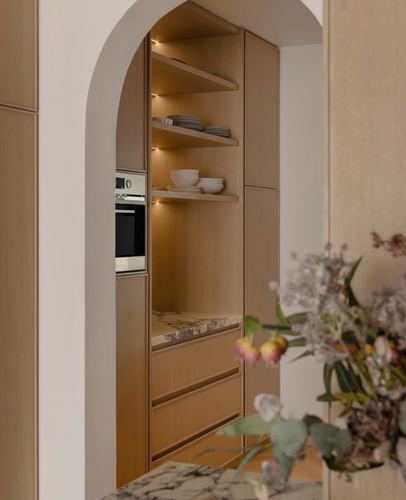 Arched doorway framing a wood kitchen with open shelving, oven, and marble backsplash