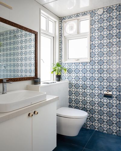 Bathroom with blue patterned tile wall, white vessel sink, and wall-hung toilet