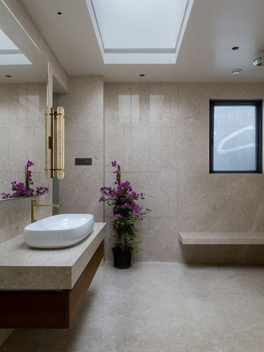 Beige stone bathroom with vessel sink, wood vanity, skylight and potted bougainvillea