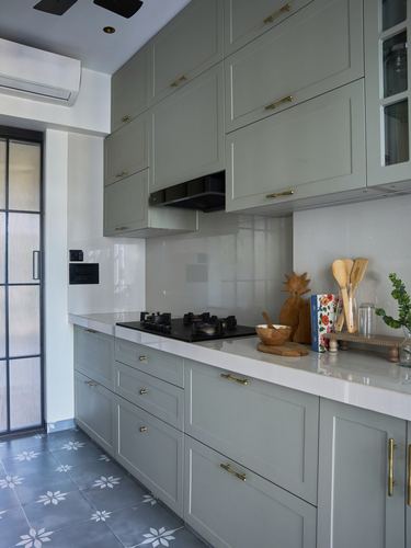 Sage green shaker kitchen with brass handles, white countertop and patterned grey tile floor