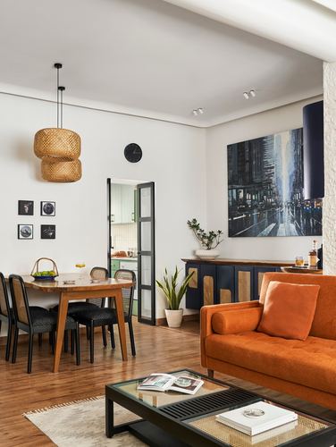 Living and dining space with orange sofa, cane sideboard, rattan pendant lights and wooden dining table
