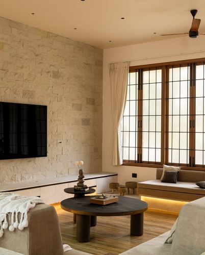 Living room with stone-clad TV wall, round black coffee table, and timber-framed window seat