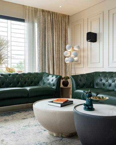 Green chesterfield sofas around fluted round marble-top coffee tables in a bright living room