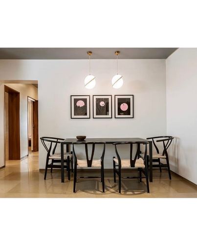 Dining room with black wishbone chairs, dark table, twin globe pendants and pink-toned art triptych